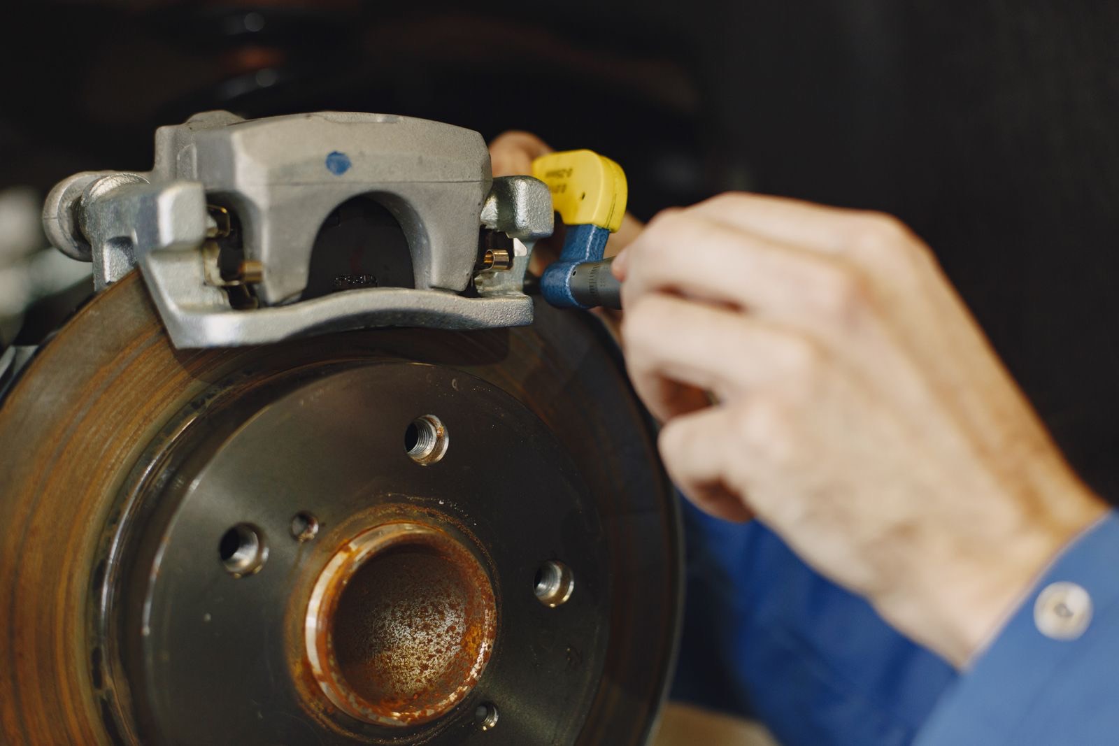 A mechanic working on a car brake disc and caliper with the wheel removed