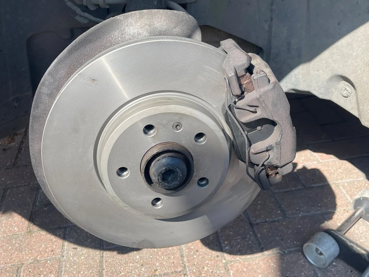 A new front brake disc fitted, its face still unmarked, with the caliper and pad back in place