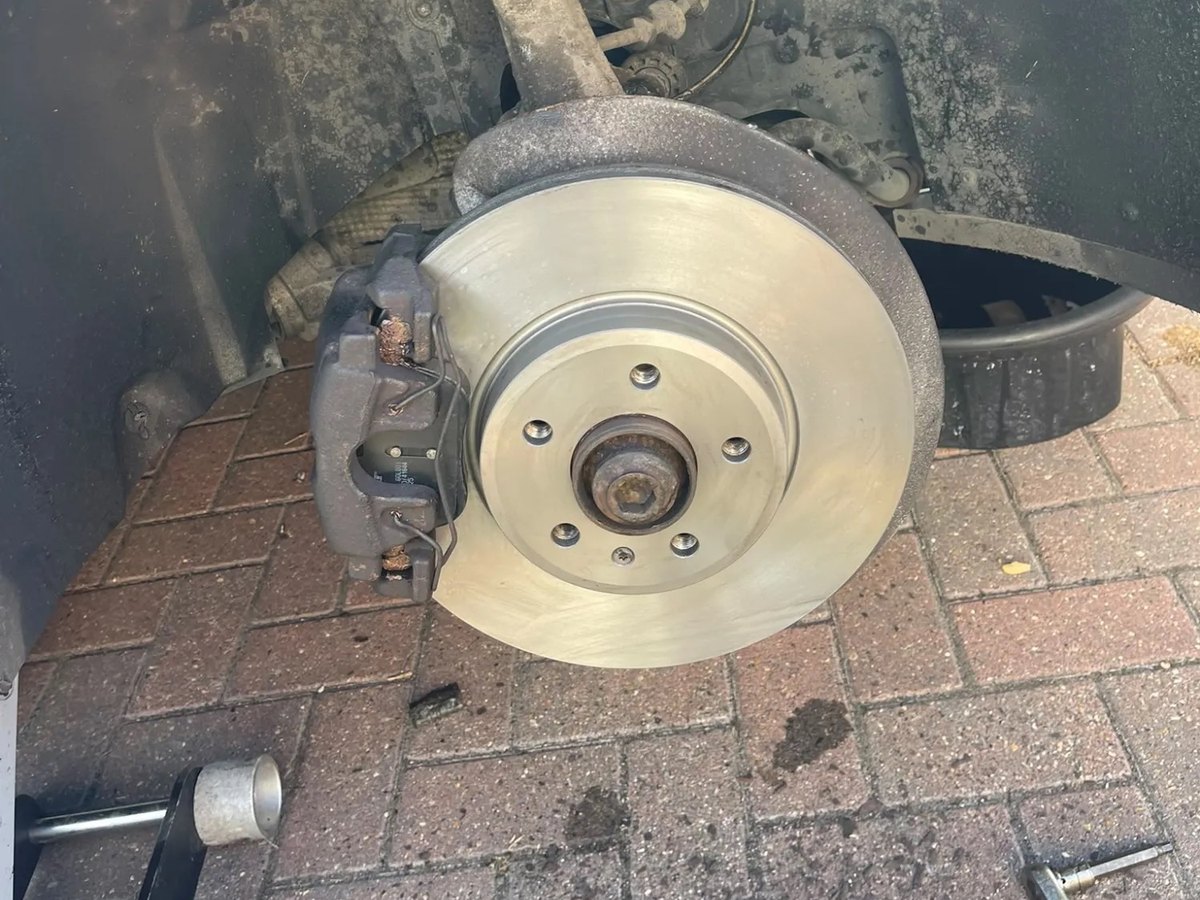 A worn front brake disc still on the car, with a raised ridge around the outer edge and the caliper alongside it