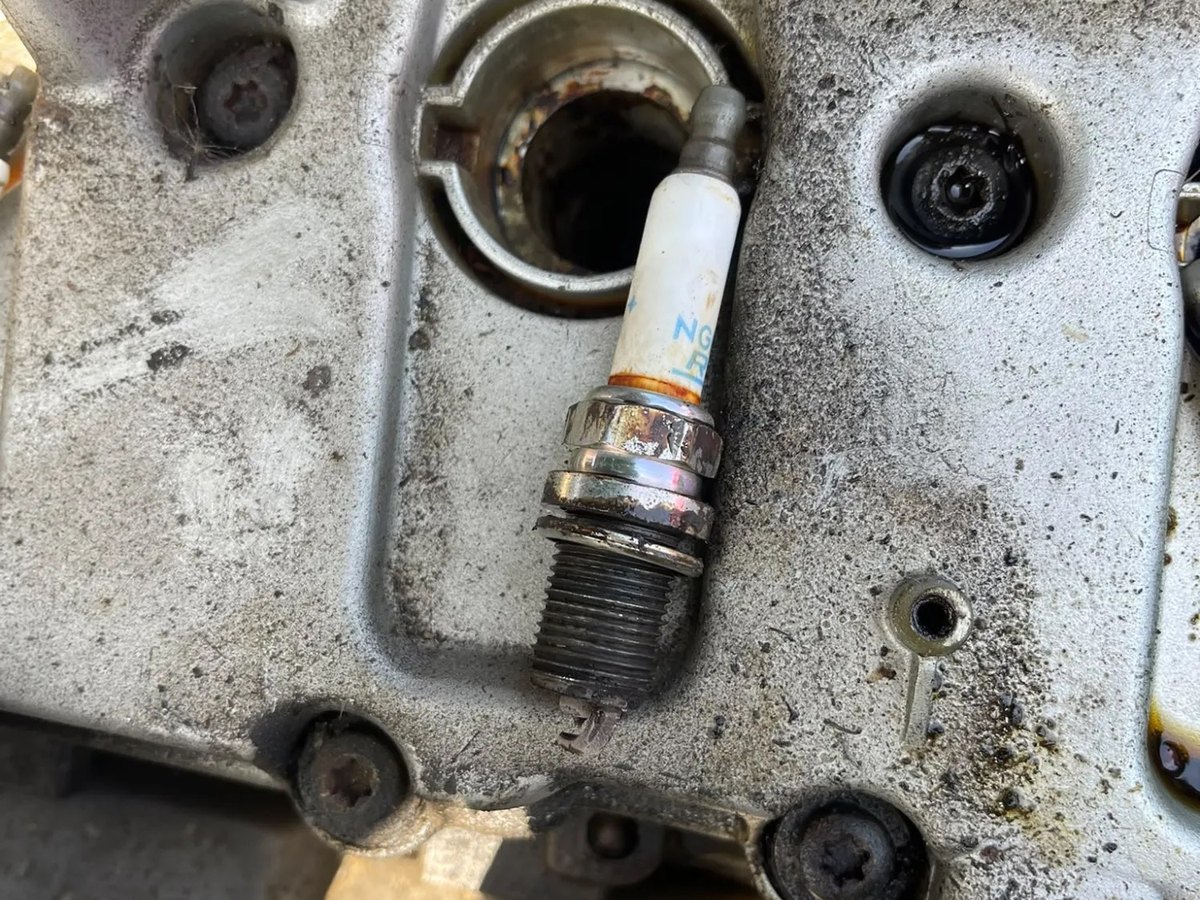 One of the old spark plugs resting on the cam cover beside the empty well it came from