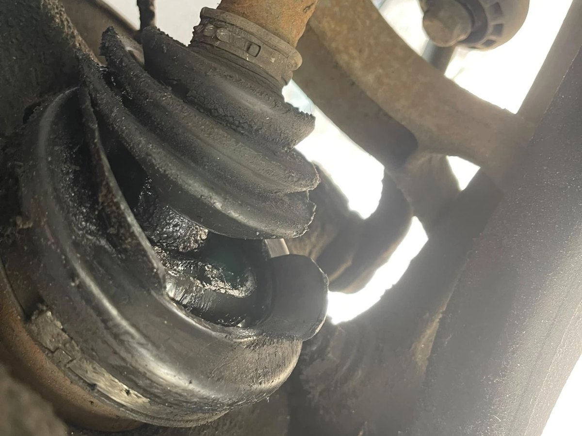 A rubber concertina boot underneath the car split open along its folds, with dark grease thrown out around the tear