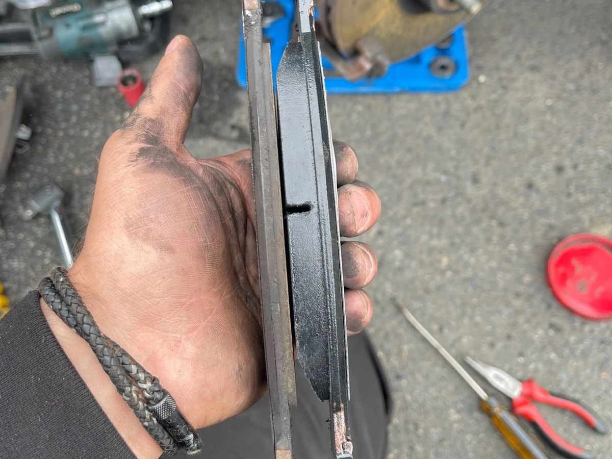 An old brake pad and a new one held edge on side by side, the old one worn down to a thin strip against the full block of the new one