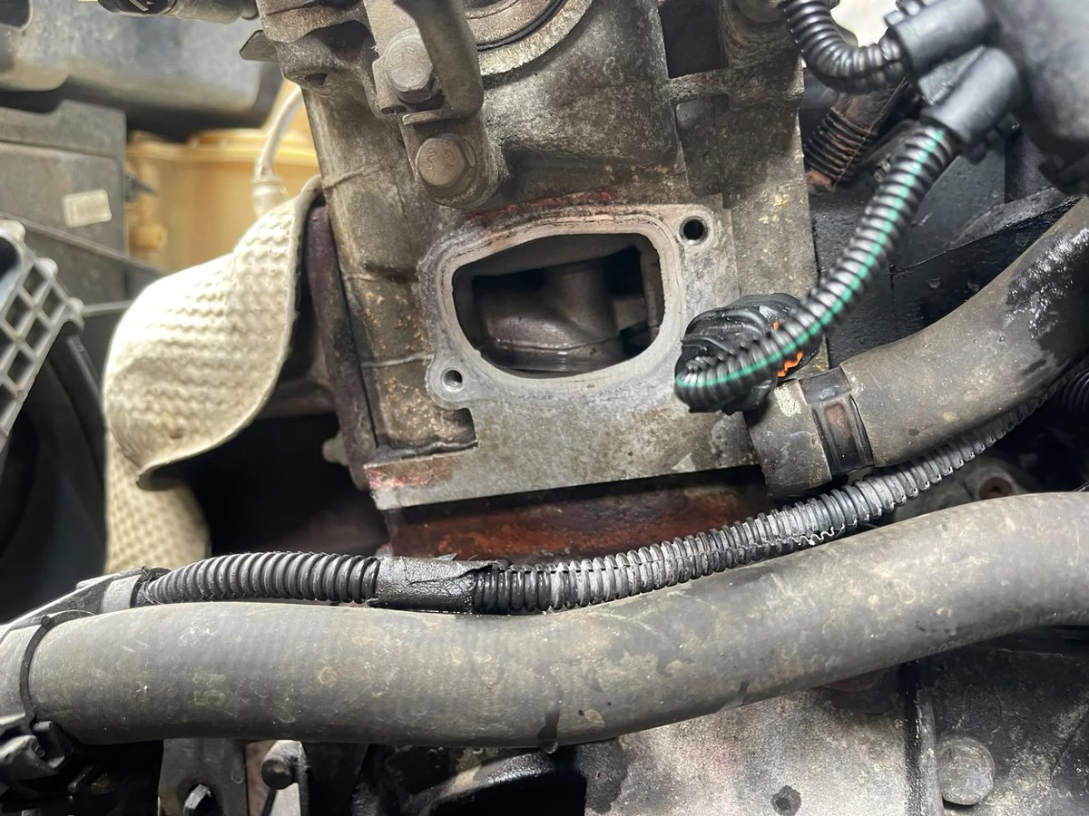 The engine with the thermostat housing removed, showing the bare mounting face and the sensor plug hanging loose beside it