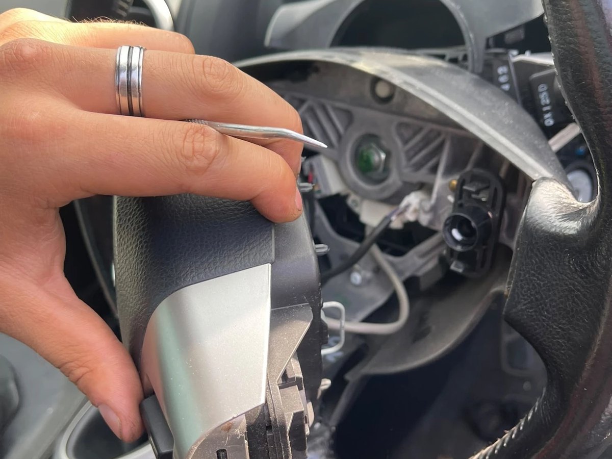The centre trim removed from a steering wheel and held clear in one hand, showing the switchgear and wiring behind it