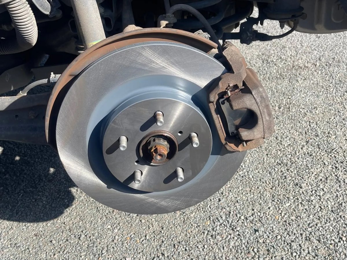 A newly fitted brake disc on the hub with the caliper swung clear beside it