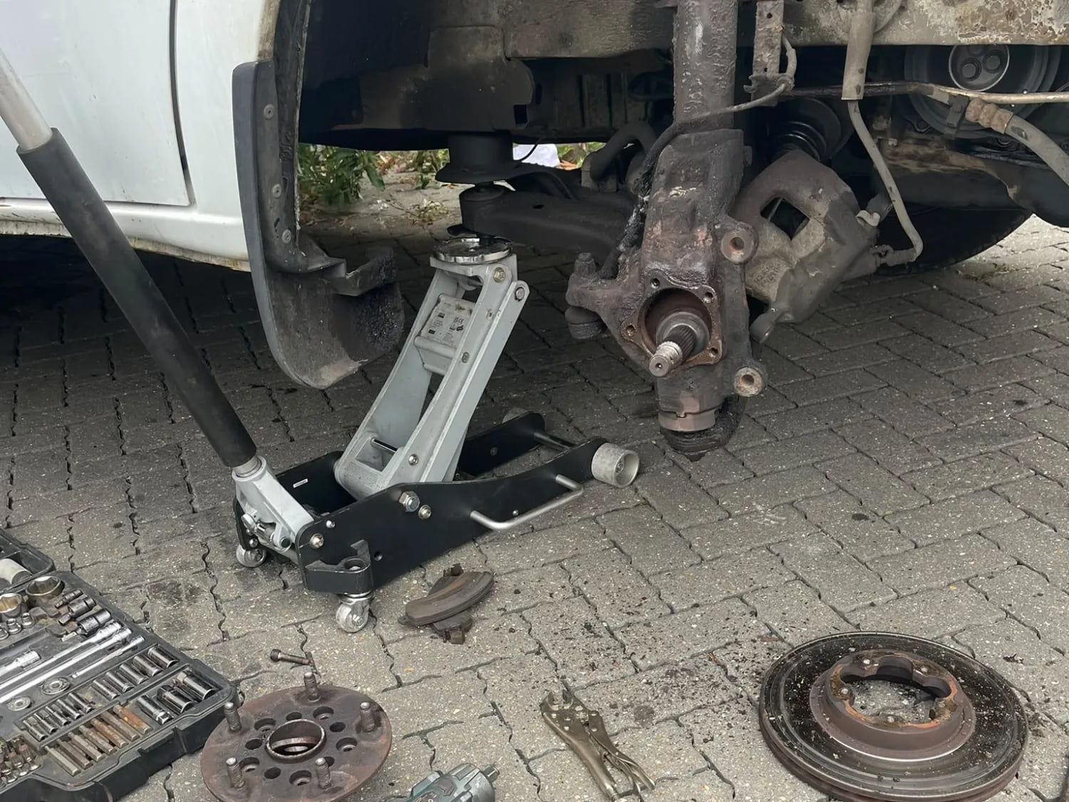 A white Ford Transit raised on a trolley jack with the front wheel off and the hub carrier exposed