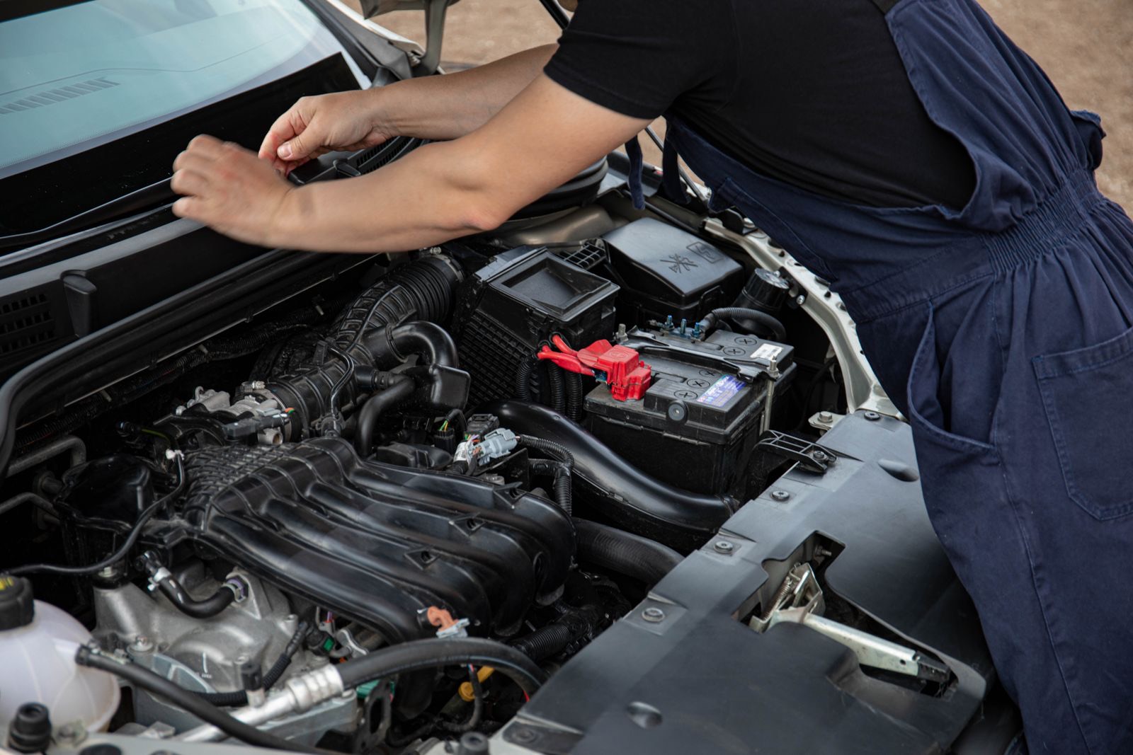 Mobile auto electrician testing a car's charging system with a multimeter under the bonnet