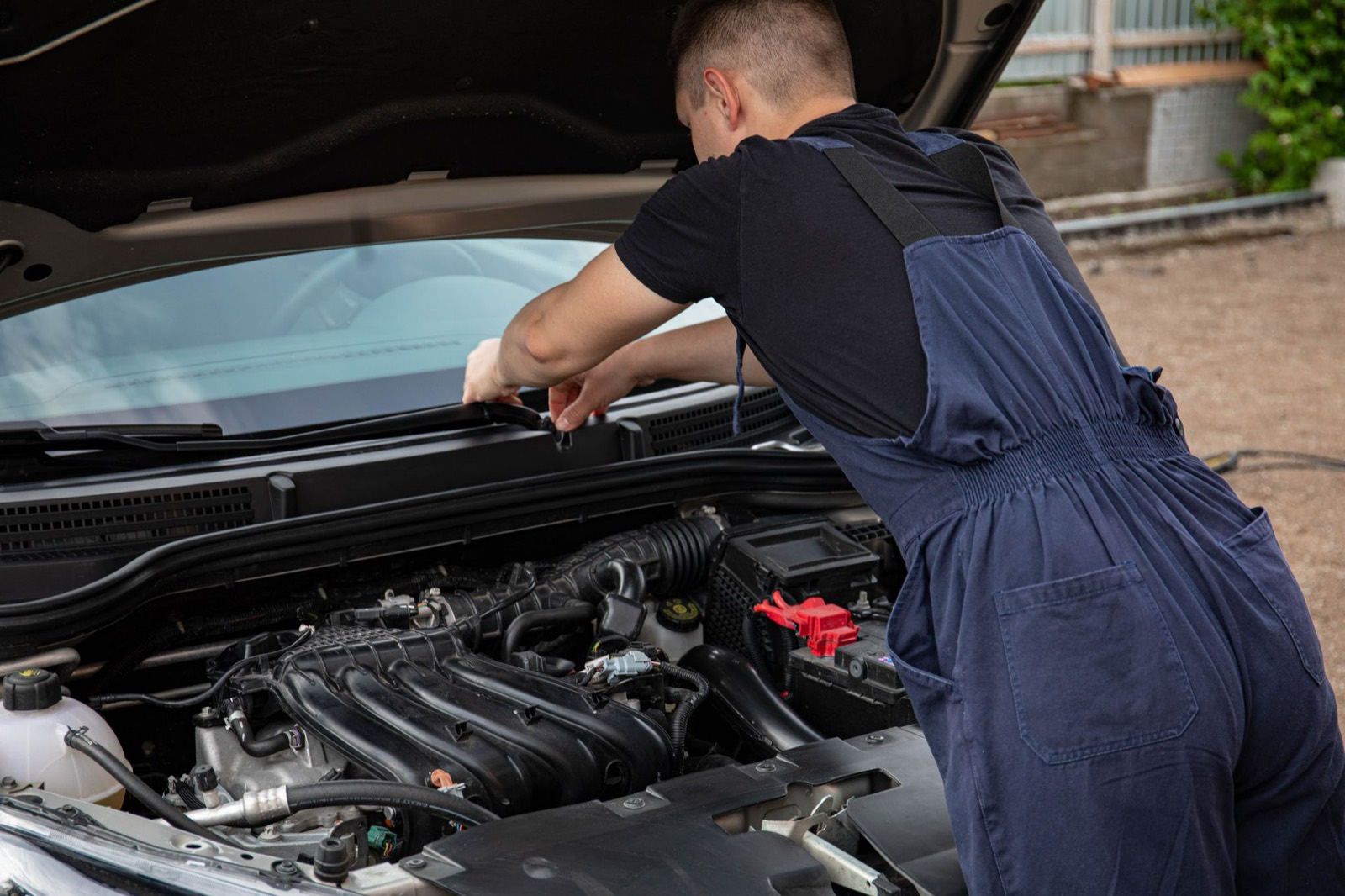 Mobile mechanic working under the bonnet of a car on a driveway